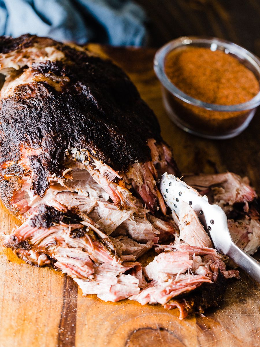 Pulled pork desmigado sobre tabla de madera, con corteza oscura